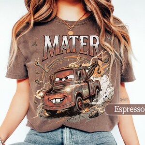 May include: Espresso-colored t-shirt featuring a cartoon image of Mater from the Cars movie. The design includes the word "MATER" in a distressed font, along with wrenches and lightning bolts. The shirt is a crew neck.