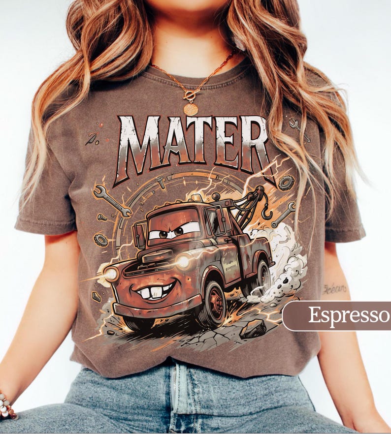 May include: Espresso-colored t-shirt featuring a cartoon image of Mater from the Cars movie. The design includes the word "MATER" in a distressed font, along with wrenches and lightning bolts. The shirt is a crew neck.