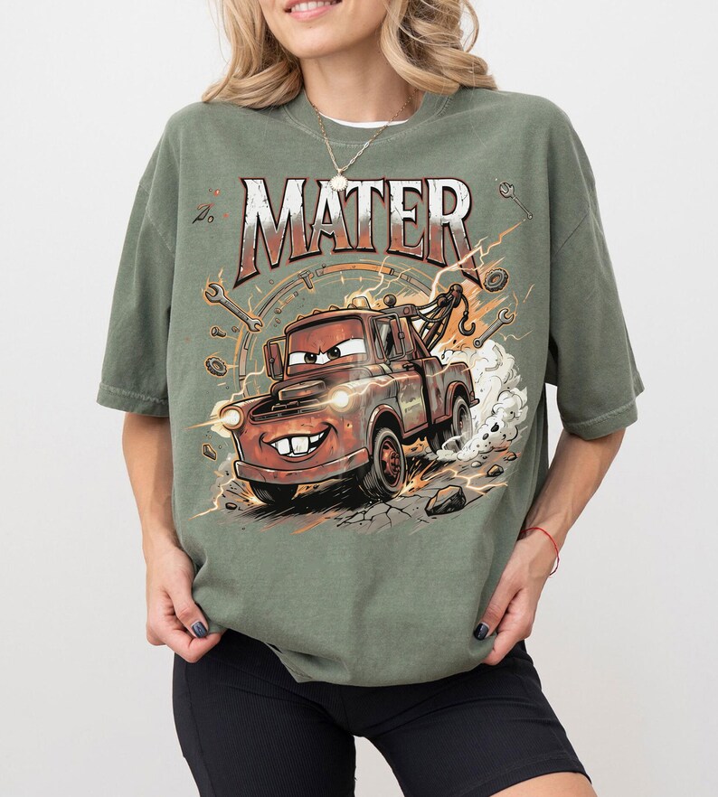 May include: Olive green t-shirt featuring a cartoon image of Mater from the movie Cars. The graphic includes the word "MATER" in a distressed font, along with tools and lightning bolts. The image depicts Mater with a big smile, driving fast.