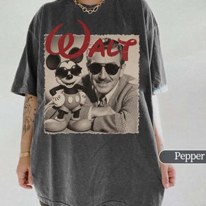 May include: Pepper-colored t-shirt featuring a sepia-toned image of Mickey Mouse and Walt Disney, with the word "Walt" in red script. Mickey is wearing sunglasses. The shirt has a relaxed fit.