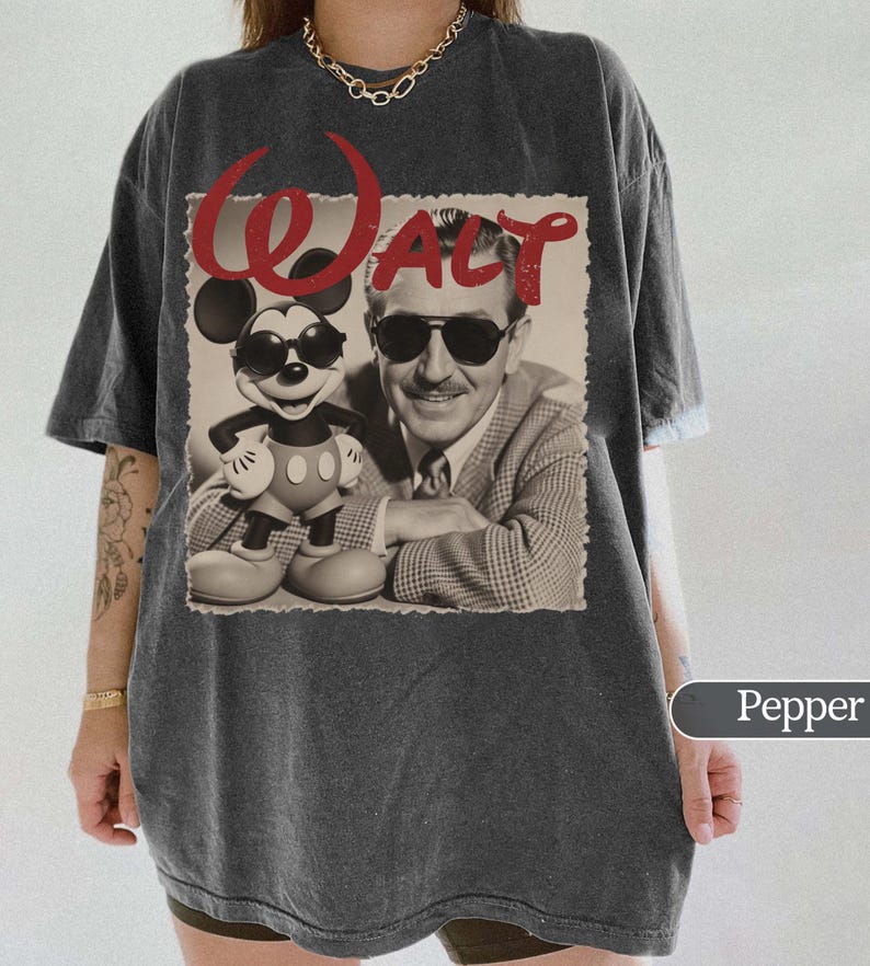 May include: Pepper-colored t-shirt featuring a sepia-toned image of Mickey Mouse and Walt Disney, with the word "Walt" in red script. Mickey is wearing sunglasses. The shirt has a relaxed fit.