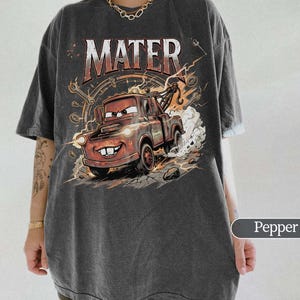 May include: Dark gray t-shirt featuring a cartoon image of Mater from the movie Cars. The graphic includes the word "MATER" in a distressed font, a smiling Mater, and a background of gears and lightning.