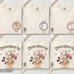 Op de afbeelding: Ivoor kleurige T-shirts met Disney-personage afbeeldingen. Ontwerpen omvatten Chip, R2-D2 en Winnie de Poeh, elk in een cirkelvormig kader met het woord "Name" eronder. Andere shirts tonen een Disney World afbeelding.