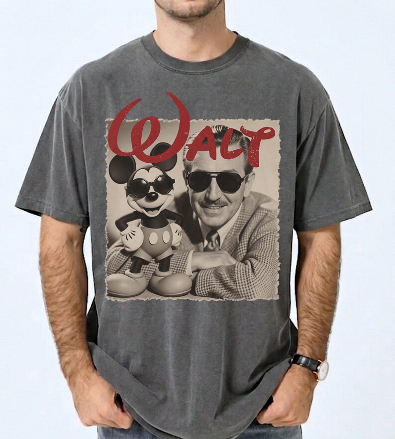 May include: Dark gray t-shirt featuring a vintage image of Walt Disney and Mickey Mouse wearing sunglasses. The word "Walt" is printed in red above the image. The shirt has a classic crew neck and short sleeves.