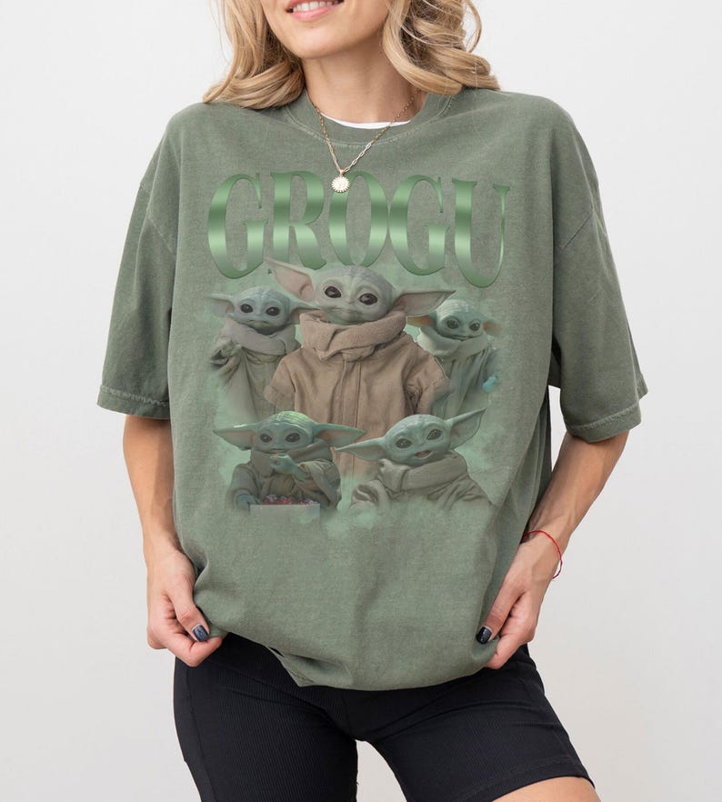 Op de afbeelding: Olijfgroen T-shirt met een afbeelding van Grogu uit The Mandalorian. Het ontwerp bevat meerdere Grogu-afbeeldingen en het woord "GROGU" in een groene, reli&euml;fletter. Het T-shirt heeft een relaxte pasvorm.