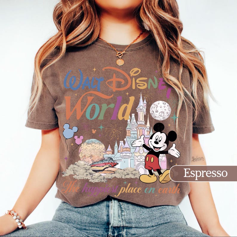 May include: Espresso-colored t-shirt featuring a colorful graphic of Mickey Mouse in front of a castle, with the words "Walt Disney World" and "The happiest place on earth". The design includes balloons, fireworks, and a planet.
