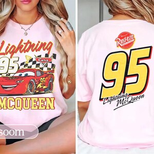 May include: Pale pink t-shirt with a graphic of Lightning McQueen from the Cars film. The front design includes the text "Lightning 95 McQueen" with a checkered flag. The back of the shirt displays a large "95" and "Lightning McQueen" text.