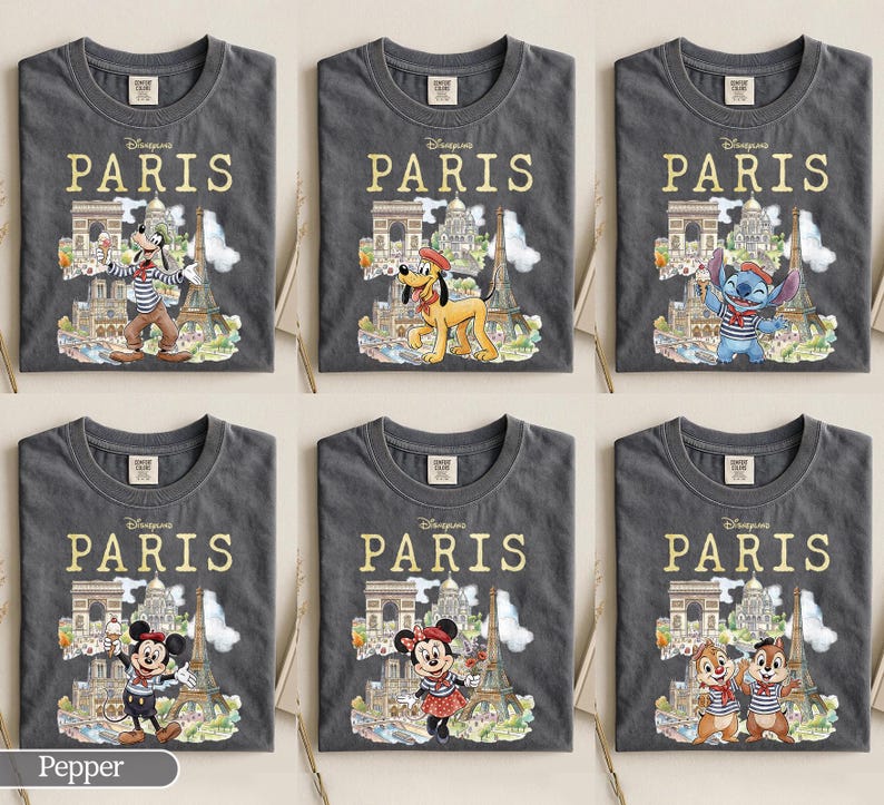 K&ouml;nnte beinhalten: Sechs graue T-Shirts mit dem Wort "PARIS" in goldfarbenen Buchstaben. Jedes Shirt zeigt eine andere Disney-Figur vor Pariser Wahrzeichen wie dem Eiffelturm und dem Arc de Triomphe. Zu den Figuren geh&ouml;ren Goofy, Pluto, Stitch, Mickey Mouse, Minnie Mouse und Chip und Chap.