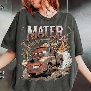 May include: Dark gray t-shirt featuring a cartoon image of Mater from the Cars movie. The word "MATER" is printed across the top in a distressed font. The graphic includes lightning bolts, wrenches, and a speedometer design.