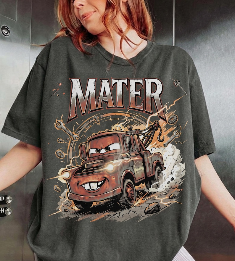 May include: Dark gray t-shirt featuring a cartoon image of Mater from the Cars movie. The word "MATER" is printed across the top in a distressed font. The graphic includes lightning bolts, wrenches, and a speedometer design.
