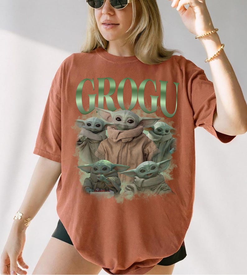 Op de afbeelding: Terracotta-kleurig T-shirt met een afbeelding van Grogu, ook bekend als Baby Yoda, uit The Mandalorian. Het woord "GROGU" is groen boven de afbeelding gedrukt. De afbeelding toont Grogu in verschillende poses.