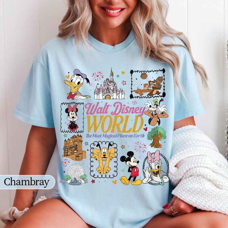May include: Light blue t-shirt featuring a colorful graphic of various Disney characters and landmarks, including Mickey Mouse, Donald Duck, and Cinderella's castle. The text "Walt Disney World" is prominently displayed.