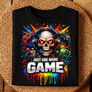 Könnte beinhalten: Schwarzes T-Shirt mit einem Totenkopf, der Kopfhörer und rote X-Augen trägt, umgeben von farbenfrohen Grafiken und Gamecontrollern. Der Text "JUST ONE MORE GAME" wird unter dem Totenkopf in einer lebendigen, tropfenden Schrift angezeigt. Ein lustiges Design für Gamer.