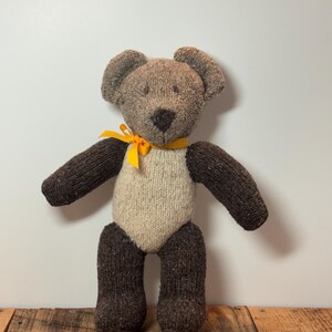 May include: A handmade teddy bear with a light brown body, dark brown limbs, and a yellow ribbon around its neck. The bear is made of knitted fabric and has a classic design, perfect for a child's toy or a decorative item.
