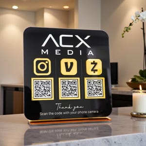 May include: A black sign with the text "ACX MEDIA" and social media icons. Below are QR codes and the text "Thank you. Scan the code with your phone camera."