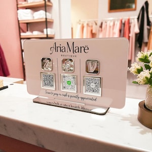 May include: Aria Mar&euml; Boutique payment display. The pink acrylic sign has three payment icons with QR codes below. The text "Scan to pay or cash is greatly appreciated" is printed on the sign.