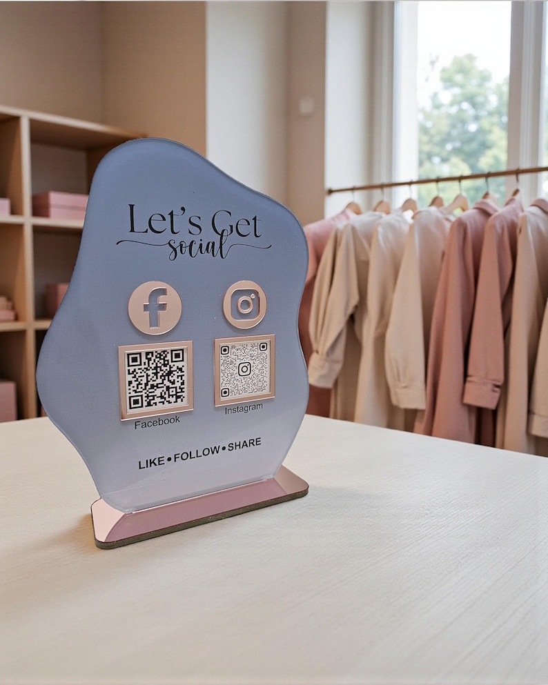 May include: A light blue social media sign with the text "Let's Get Social". It features Facebook and Instagram icons with corresponding QR codes. The base is pink, and the sign says "LIKE &bull; FOLLOW &bull; SHARE".
