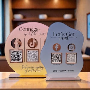 May include: Two acrylic social media signs. One is a circle with a gradient of pink and yellow, the other is an abstract shape in blue and gray. Both have social media icons, QR codes, and text that says "Connect with us" and "Let's Get Social".