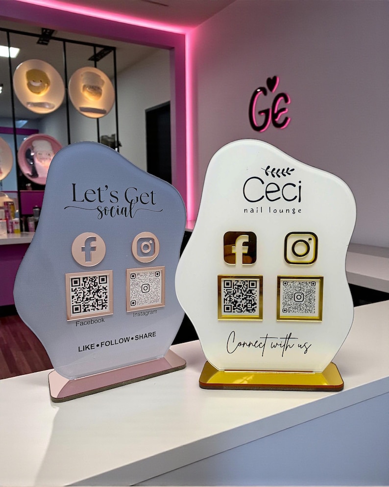 May include: Two decorative social media signs for a nail lounge. One is light blue with the text "Let's Get Social" and the other is white with the text "Ceci nail lounge". Both have Facebook and Instagram icons with QR codes.