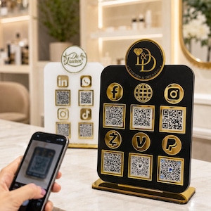 May include: A black rectangular social media sign with gold accents, featuring a circular logo at the top with the text Diamonds & Dreams, and a grid of gold-framed icons and QR codes for Facebook, Instagram, PayPal, and other digital platforms.
