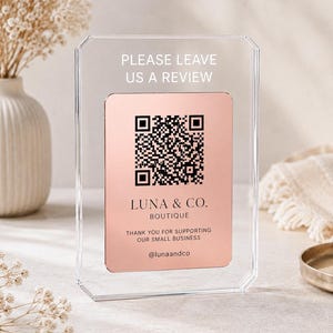Puede incluir: Un letrero de acrílico transparente con un inserto en oro rosa y un código QR negro. El texto dice: PLEASE LEAVE US A REVIEW, LUNA & CO. BOUTIQUE, THANK YOU FOR SUPPORTING OUR SMALL BUSINESS y @lunaandco. El letrero tiene forma rectangular.