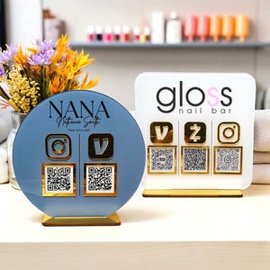 May include: Two acrylic business signs. One is a blue circle with the name "NANA" and social media icons. The other is a white rectangle with "gloss nail bar" and social media icons. Both have gold accents and QR codes.