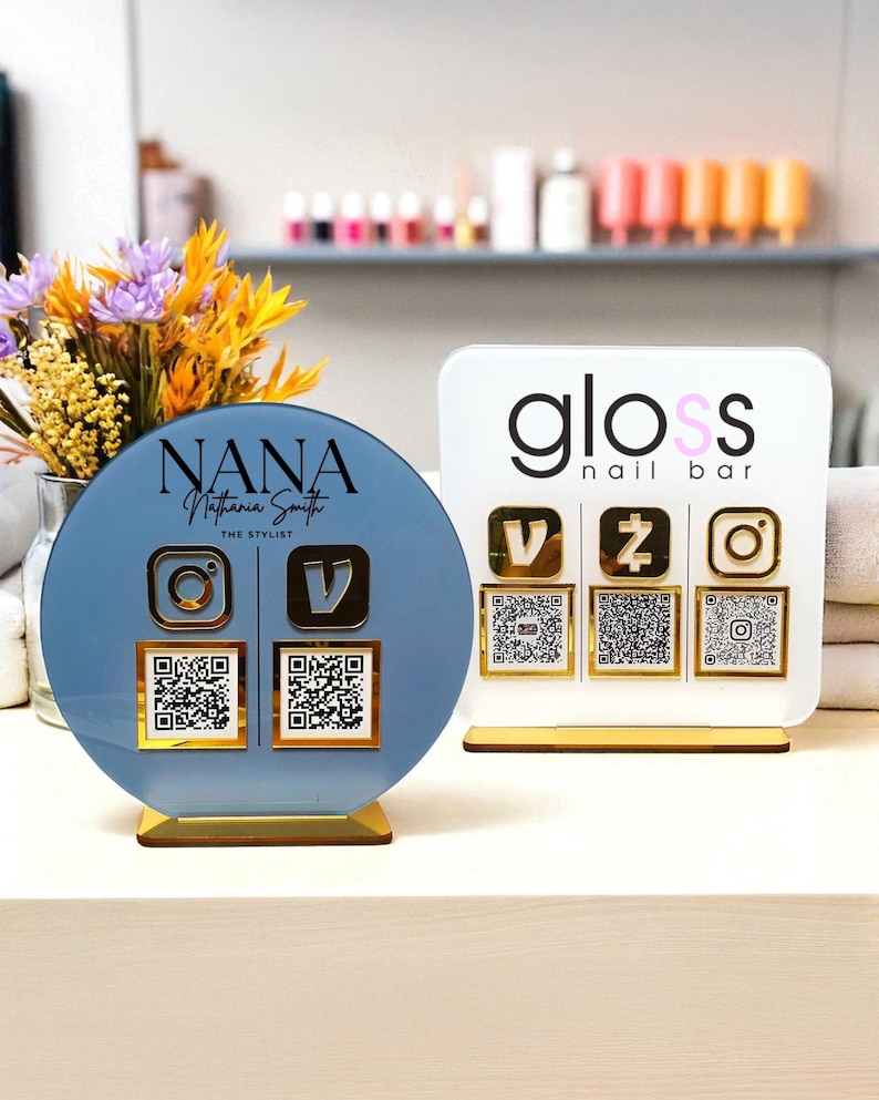 May include: Two acrylic business signs. One is a blue circle with the name "NANA" and social media icons. The other is a white rectangle with "gloss nail bar" and social media icons. Both have gold accents and QR codes.