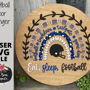 Puede incluir: Un colgador de puerta redondo de madera con un diseño de arcoíris con balones de fútbol, un casco de fútbol y el texto "Eat, Sleep, Football".