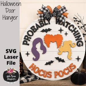 May include: A round white wooden door hanger featuring the black text PROBABLY WATCHING and orange text HOCUS POCUS. It includes three colorful hair silhouettes in purple, orange, and yellow, black bat and star cutouts, and a plaid bow on top.