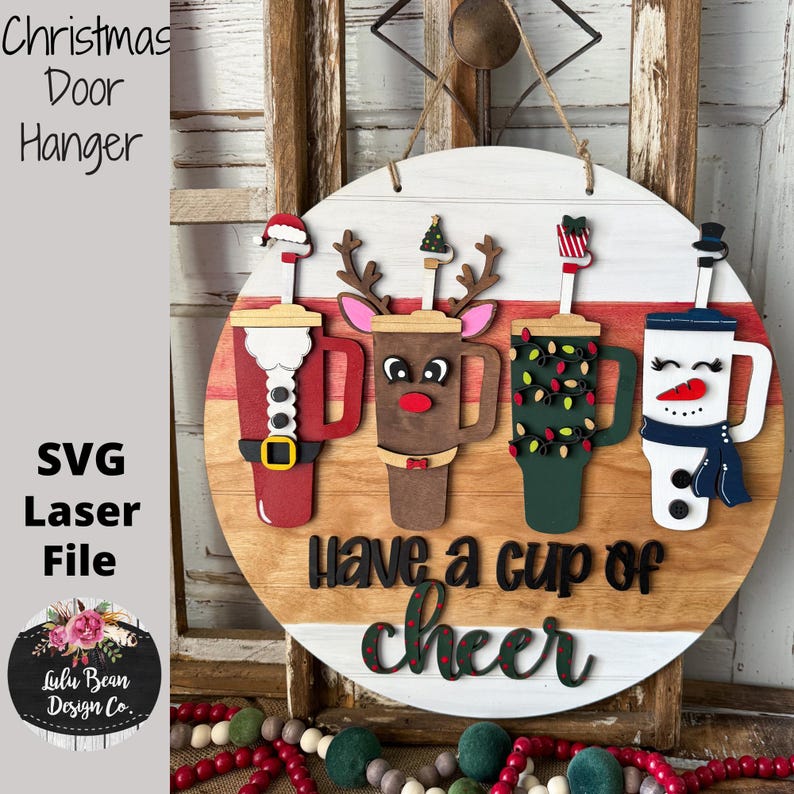 Pode incluir: Cabide de porta de Natal em madeira com quatro desenhos de canecas de caf&eacute; festivas: Papai Noel, rena, uma caneca com luzes de Natal e um boneco de neve. O texto "Have a cup of cheer" est&aacute; abaixo. Arquivo a laser.