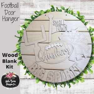 May include: A wooden football-themed door hanger kit. The round, unfinished wood piece features cut-out designs of a football, goalpost, and pom-pom, with the words "Huskers", "Big Spirit", and "Small Town". The words "Football Door Hanger" and "Wood Blank Kit" are also visible.
