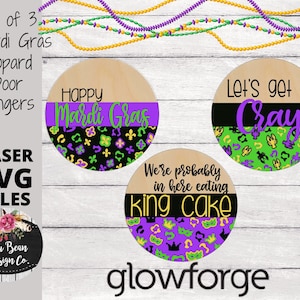 May include: Set of three Mardi Gras themed round wooden door hangers. The first hanger says "Happy Mardi Gras" in purple and green lettering on a black and gold background. The second hanger says "Let's get Cray" in purple lettering on a black and green background. The third hanger says "We're probably in here eating king cake" in black lettering on a purple and gold background.