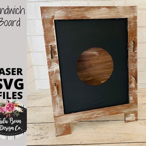 以下が含まれることがあります： 黒板のインサートと円形の切り抜きが付いた、素朴な木製のサンドイッチボード。ボードは木製のイーゼルに置かれ、白く塗られた風合いがあります。