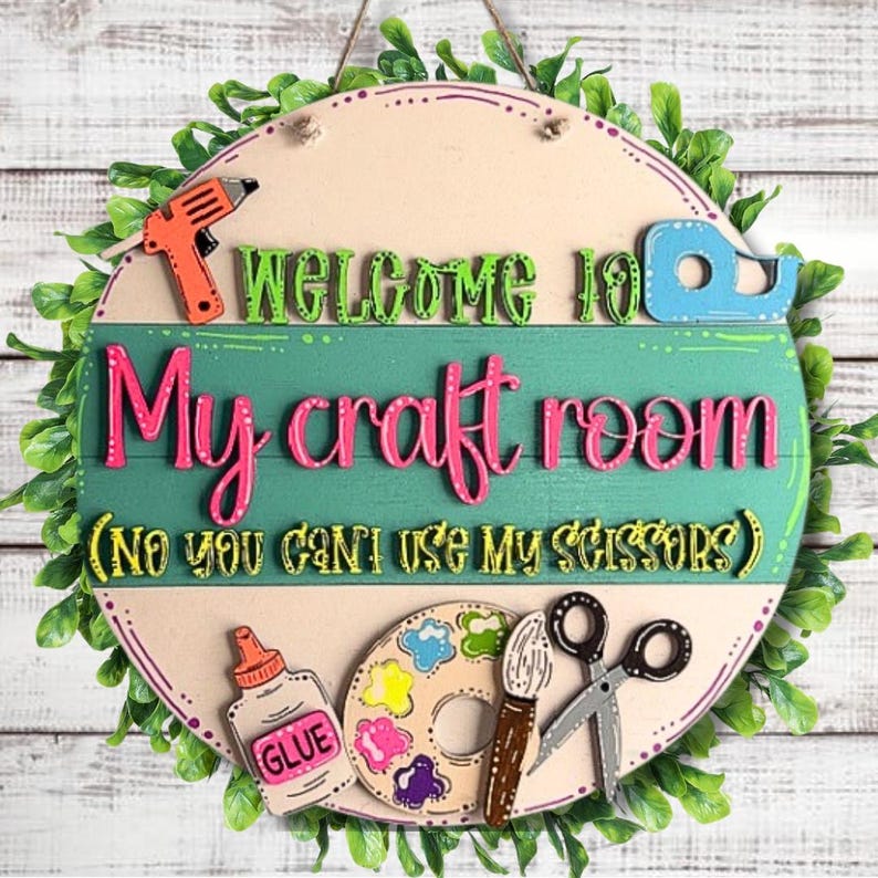 May include: A round wooden sign with the text "WELCOME TO My craft room (NO YOU CAN'T USE MY SCISSORS)". The sign features craft supplies like glue, a paintbrush, scissors, and a paint palette. Green leaves surround the sign.