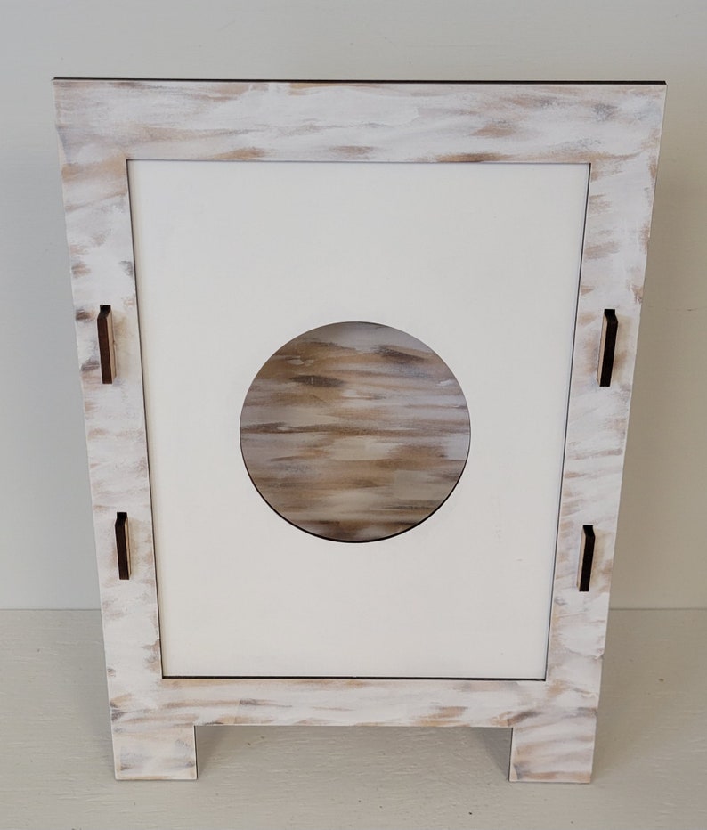 Op de afbeelding: Wit houten kastje met een ronde uitsparing en een verweerde verfbehandeling. Het kastje heeft vier kleine houten pootjes.