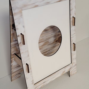 Op de afbeelding: Een witte houten ezel met een ronde uitsparing in het midden. De ezel heeft een witte geverfde afwerking met een houtnerfstructuur.