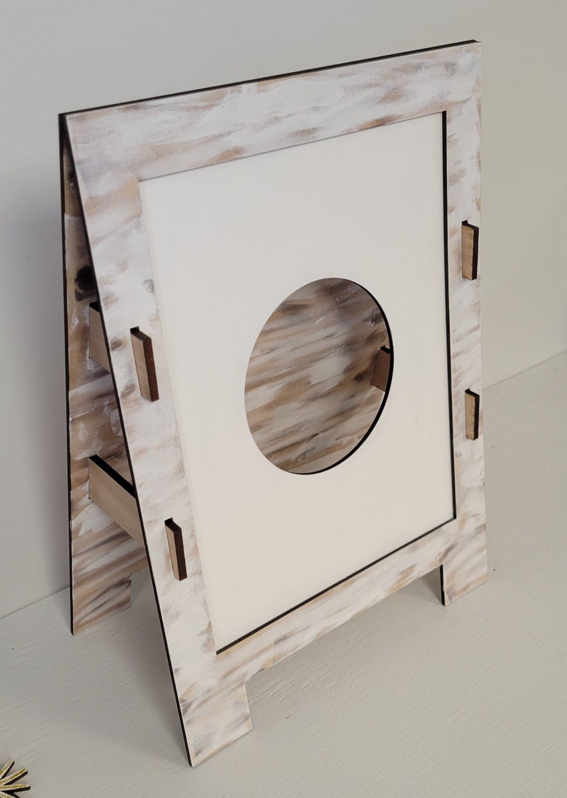 Op de afbeelding: Een witte houten ezel met een ronde uitsparing in het midden. De ezel heeft een witte geverfde afwerking met een houtnerfstructuur.