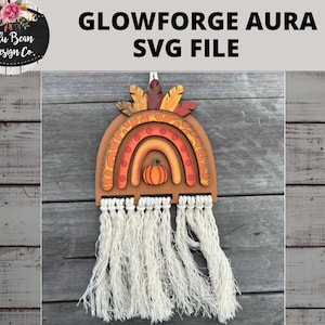 Op de afbeelding: Een houten regenboog met een herfstthema. De regenboog is geschilderd in tinten oranje, geel en bruin. In het midden van de regenboog is een kleine pompoen. De regenboog hangt aan een witte kwast.