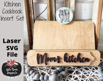Könnte beinhalten: Ein Holz-Kochbuchständer mit einem Laser-Schnitt-Design, das "Mom's Kitchen" sagt. Der Ständer hat einen Teller mit einer Gabel, einem Messer und einem Löffel. Der Ständer steht auf einem Tisch mit grauen Perlen.
