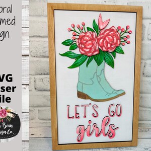 May include: A wooden framed sign with a light blue boot filled with pink flowers and the text "Let's go girls" in pink.