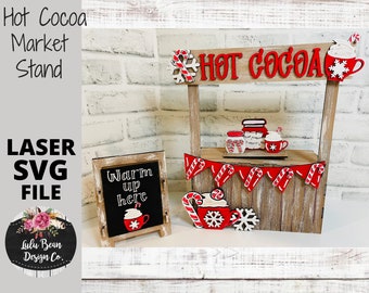 Könnte beinhalten: Ein Holzstand für heiße Schokolade mit einem roten Schild, auf dem "Hot Cocoa" steht. Der Stand hat ein Schild aus Schiefer, auf dem "Warm up here" steht, und eine Girlande aus roten und weißen Zuckerstangen. Der Stand ist mit roten und weißen Zuckerstangen, Schneeflocken und einer Tasse heißer Schokolade verziert.