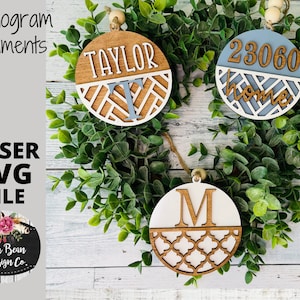 Op de afbeelding: Drie houten ornamenten met een witte achtergrond en een bruin geometrisch patroon. De bovenste ornament zegt "TAYLOR" in witte letters. De middelste ornament zegt "23060 home" in witte letters. De onderste ornament heeft een grote "M" in bruine letters.