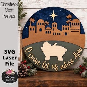 May include: A circular wooden wall sign featuring a layered nativity scene with a dark blue starry sky, a golden star, brown buildings, and a light wood manger silhouette. The text O come let us adore Him is written in cursive script.