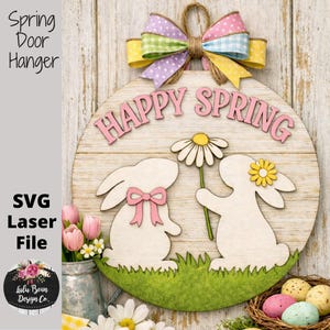 Op de afbeelding: Een houten lente deurbord met een kleurrijke strik en de woorden "Happy Spring". Het ronde bord heeft twee konijn silhouetten, een groene grasbasis en een madeliefje. Het bord heeft ook de tekst "SVG Laser File."