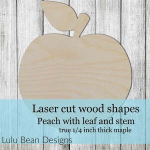 May include: Laser cut wood shape of a peach with a leaf and stem. The peach is made of 1/4 inch thick maple wood. "Laser cut wood shapes Peach with leaf and stem true 1/4 inch thick maple Lulu Bean Designs" is printed below the peach.