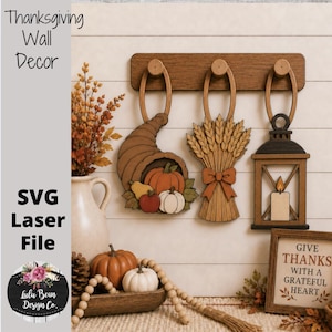 May include: A wooden wall rack with three hanging ornaments: a cornucopia with pumpkins, a wheat sheaf with a bow, and a lantern with a candle. Below, a wooden sign reads "GIVE THANKS WITH A GRATEFUL HEART" alongside pumpkins and a vase.