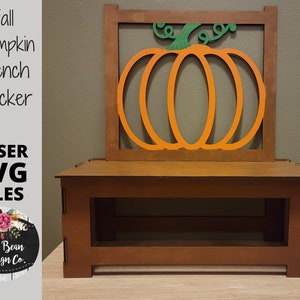 Könnte beinhalten: Ein hölzerner Bankrücken mit einem großen orangefarbenen Kürbisausschnitt und grünen Stiel und Blättern. Der Bankrücken hat einen rechteckigen Rahmen und ist aus braunem Holz gefertigt. Auf der linken Seite steht "Fall Pumpkin Bench Backer" und "LASER SVG FILES".
