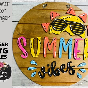 May include: A wooden round door hanger with the words "Summer Vibes" in black lettering. The word "Summer" is in colorful letters with a yellow sun with sunglasses above it.