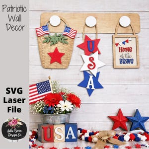 May include: Patriotic wall decor featuring a wooden basket with American flags, star-shaped ornaments spelling "USA", and a framed sign reading "Home of the Brave." A floral arrangement and star-shaped decorations complete the display.