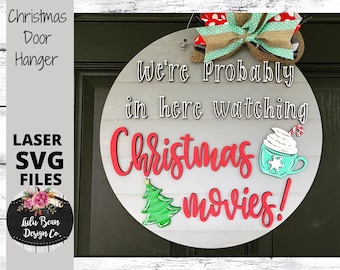 May include: A round wooden sign with the text "We're Probably in here watching Christmas movies!" in white lettering. The sign is decorated with a red and white bow, a green Christmas tree, and a blue and white mug with whipped cream and a candy cane.